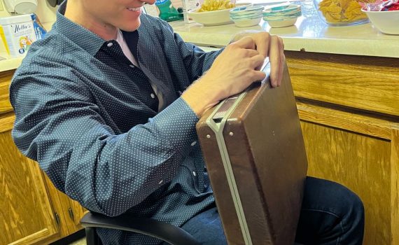 Student sitting in chair lock picking a briefcase.